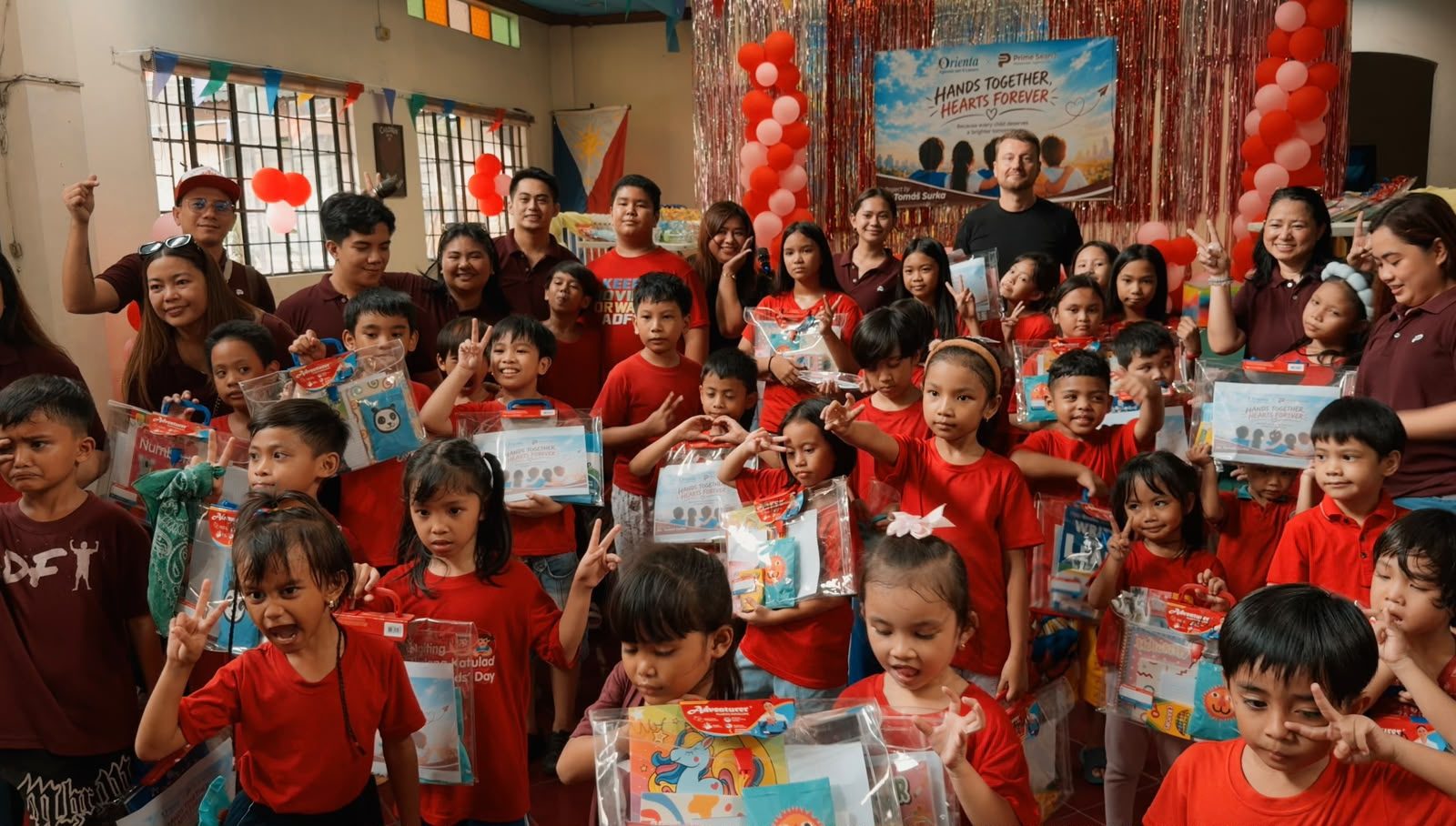 Children holding school-supply packs together with the Prime Search team at the first Hands Together, Hearts Forever visit in the Philippines